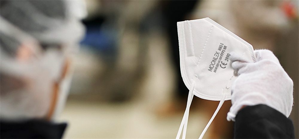 A gloved MOONLEX technician inspecting a finished respirator on the production floor